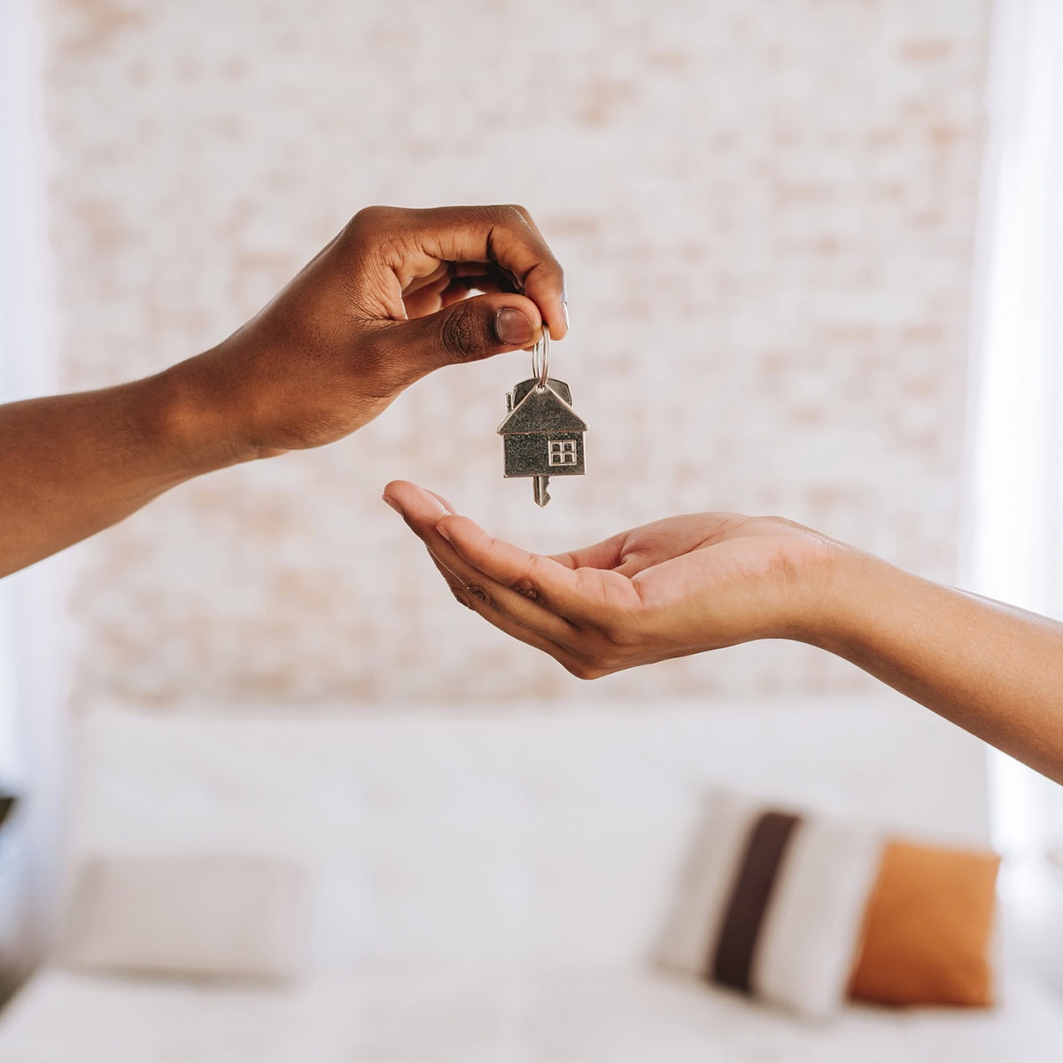 A hand handing a house-shaped key to another hand in front of a couch
