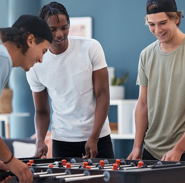 Three male college students playing foosball in a community area